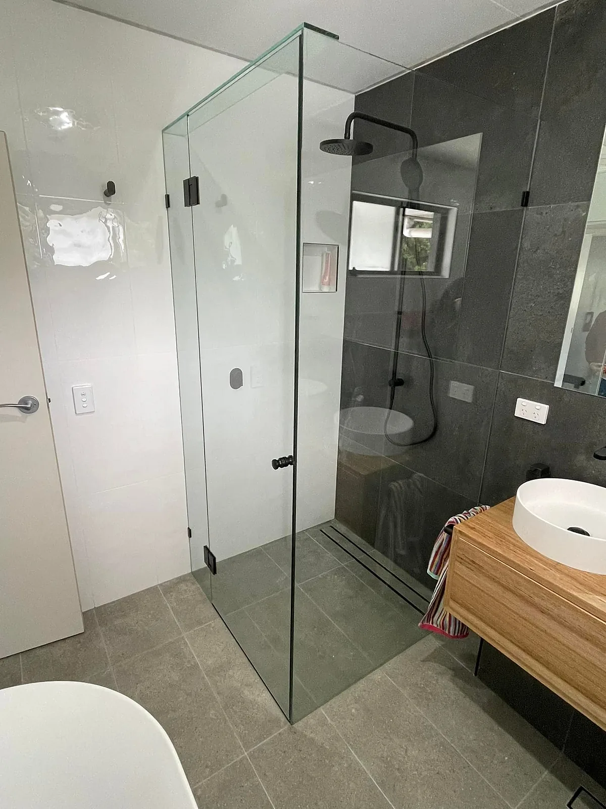 Frameless glass shower with black fittings beside a timber floating vanity