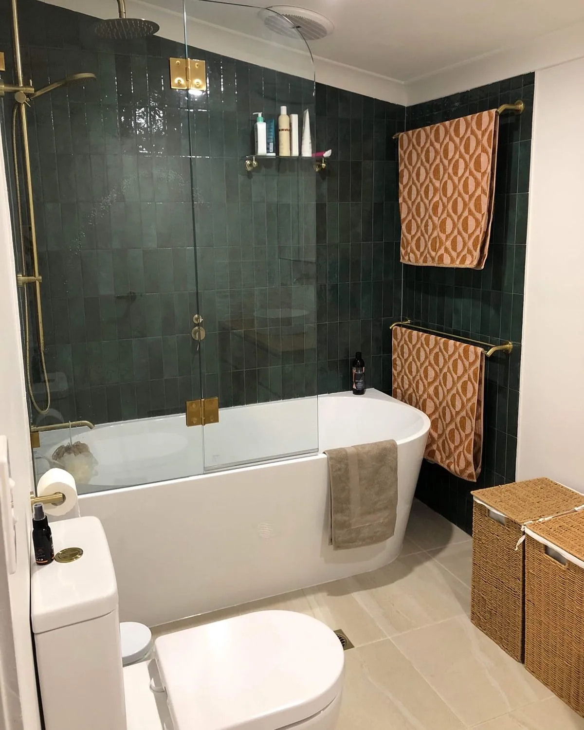 Bathroom in dark green tile with brushed brass fittings, a freestanding bath and woven baskets