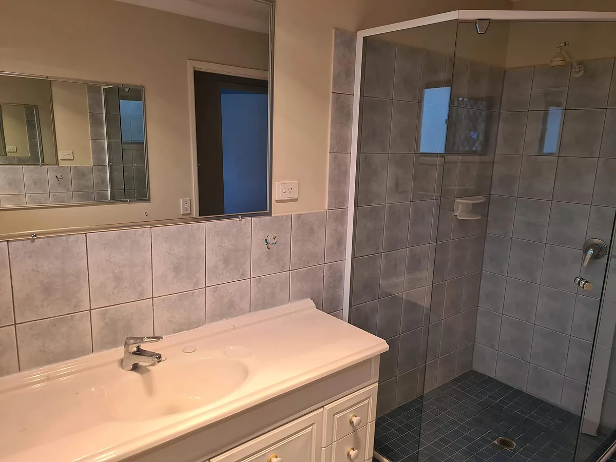 Bathroom with grey tiles, a glass shower screen and a white vanity