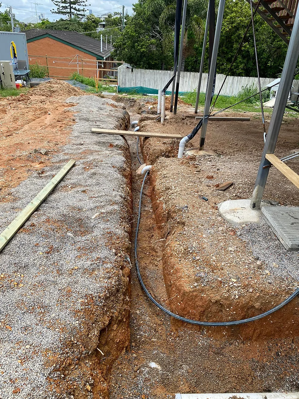 Open trench under a house with new drainage pipe and poly water line laid in