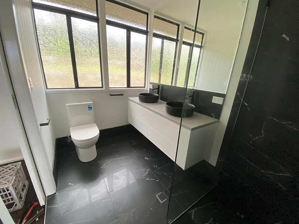 Finished bathroom with black marble-look tiles, a floating white vanity with twin black basins and bright windows