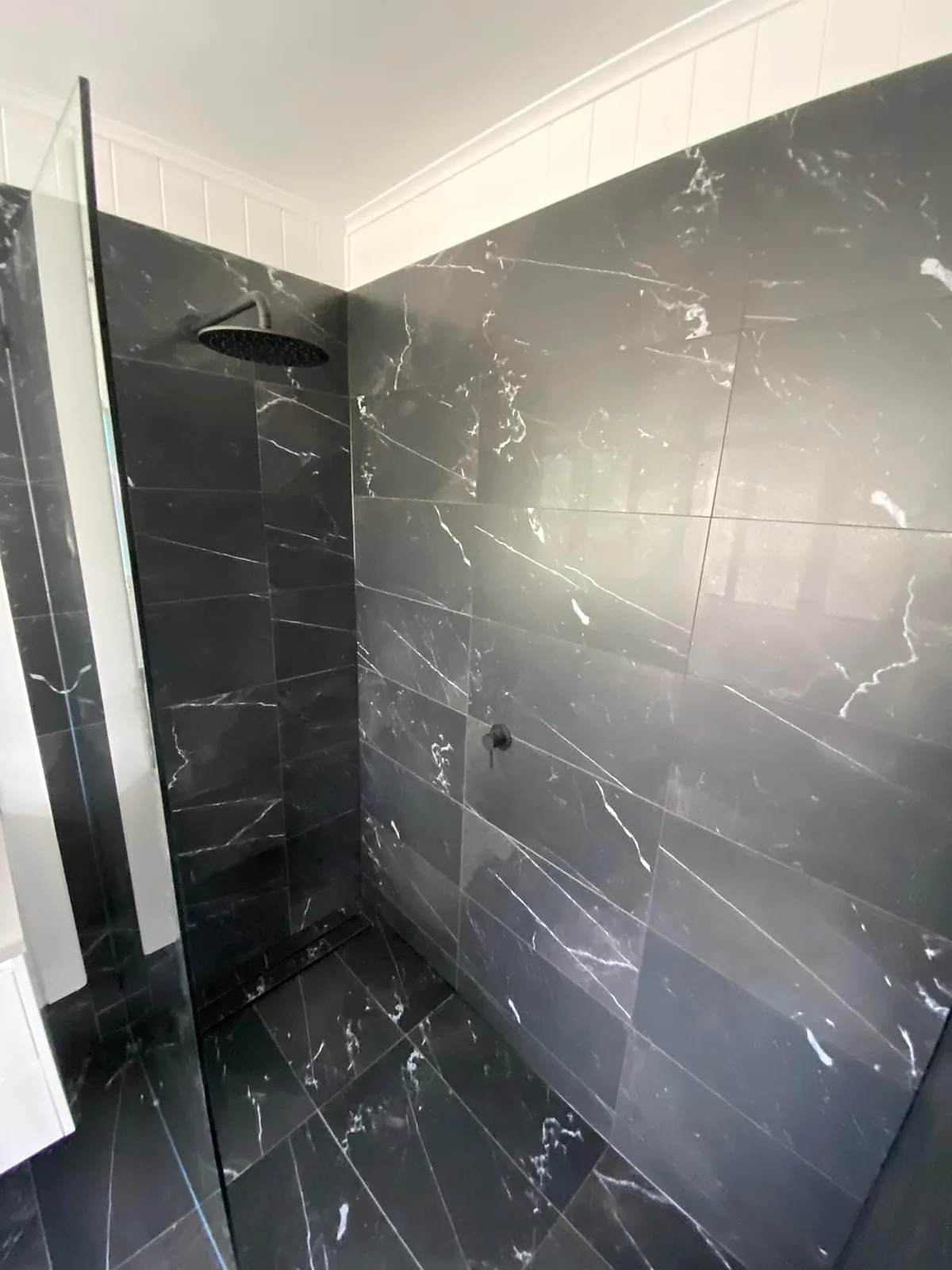 Dark marble-look tiled shower with a black rain head