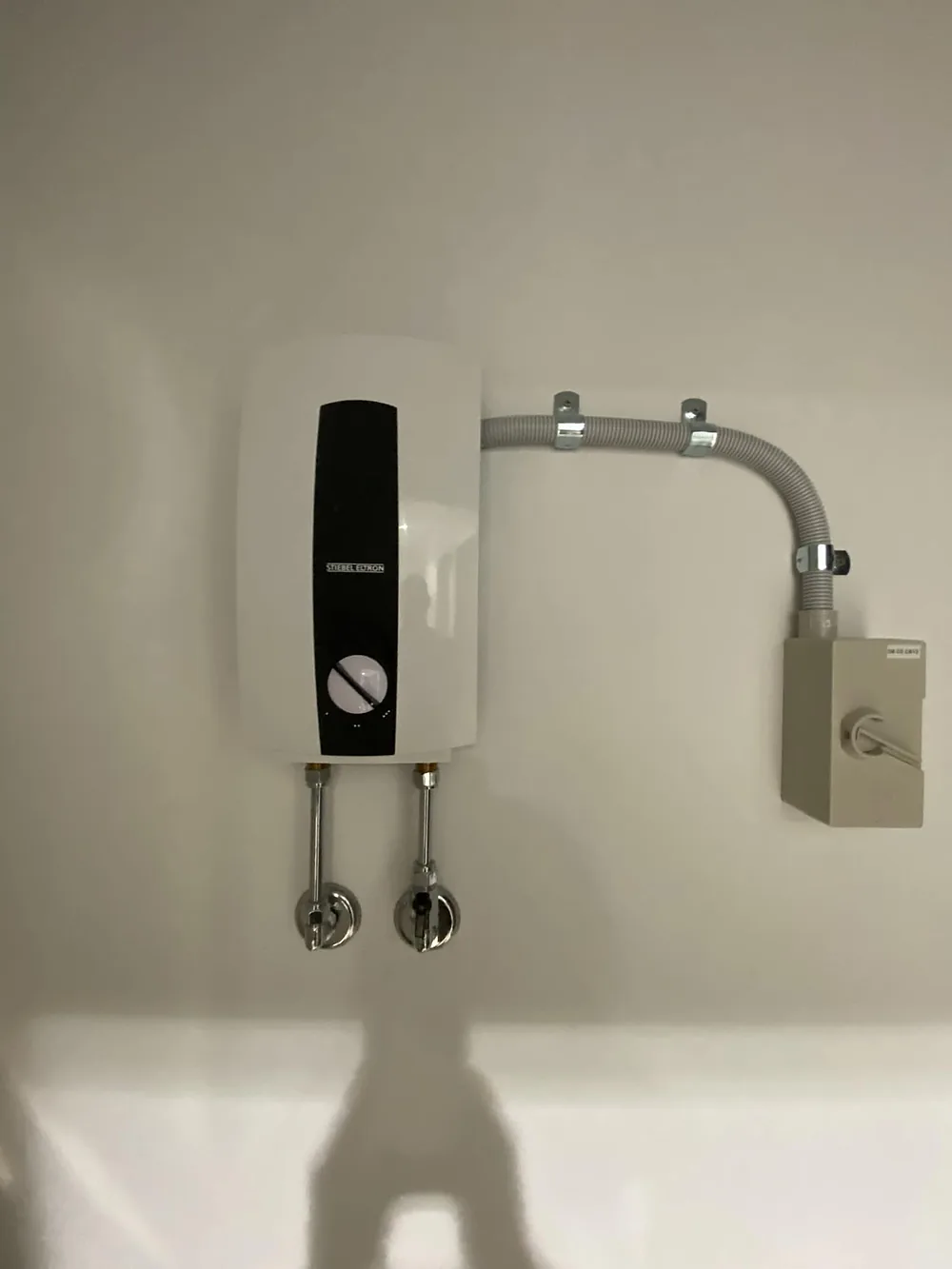 Stiebel Eltron instantaneous water heater mounted on a white wall with neat conduit and valves